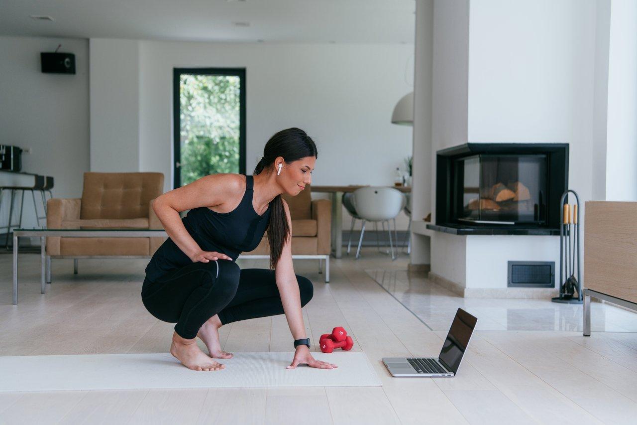 Coach sportif corrige la posture d’une novice en squats lors d’un entraînement home fitness coaching à domicile.