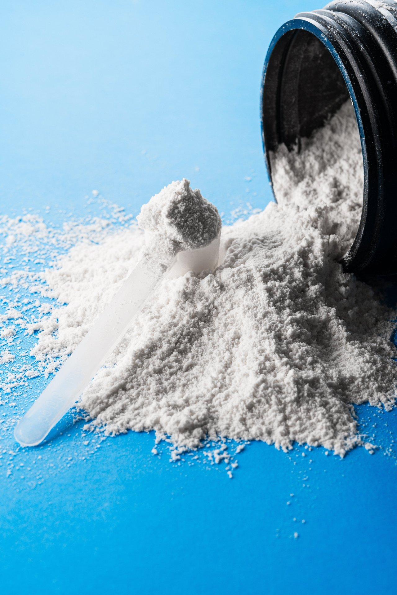 Pot de créatine monohydrate en poudre pour la récupération musculaire après musculation intensive, à côté d’une bouteille d’eau.